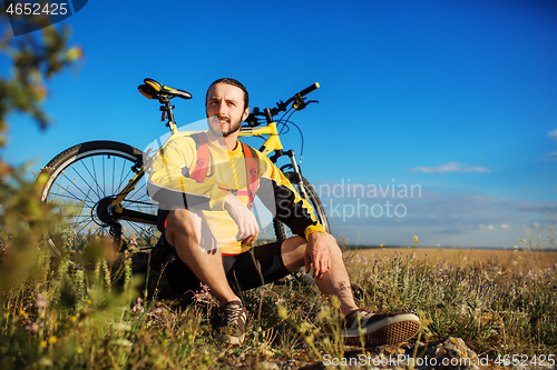 Image of Cyclist resting on grass in mountains. Man is looking aside.