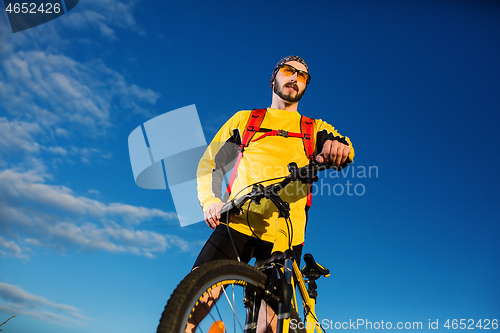 Image of Cyclist man standing on top of a mountain with bicycle