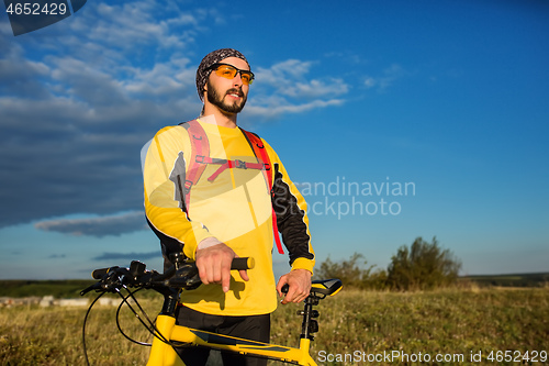 Image of Cyclist man standing on top of a mountain with bicycle