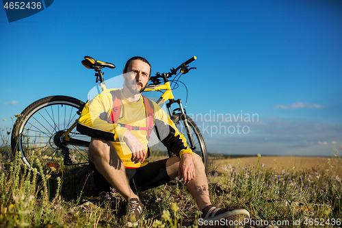 Image of Cyclist resting on grass in mountains. Man is looking aside.