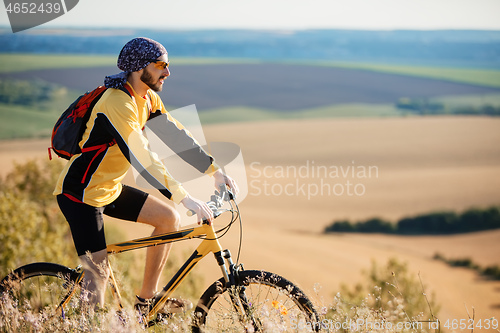 Image of Cyclist riding a bike on off road to the sunset