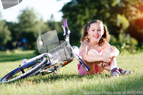 Image of Portrait of girl with bicycle. Trees on background.