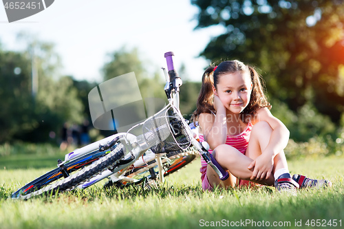 Image of Portrait of girl with bicycle. Trees on background.