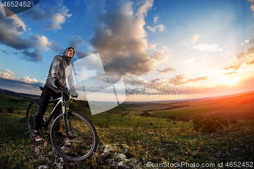 Image of Young man cycling in a summer meadow at sunset