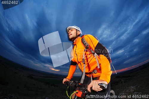 Image of Man in helmet stay on bicycle under sky with clouds.