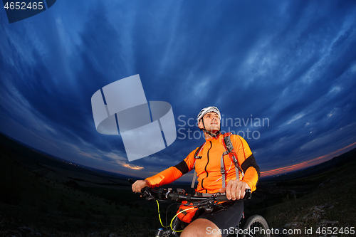 Image of Man in helmet stay on bicycle under sky with clouds.