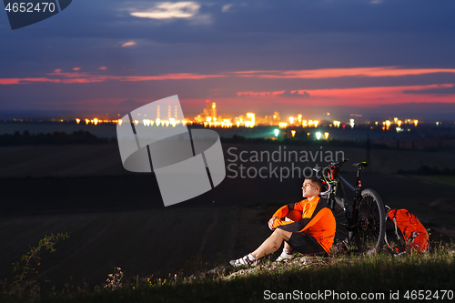Image of Cyclist resting on grass in mountains. Man is looking aside.