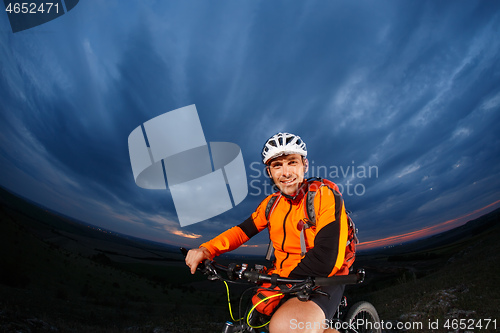 Image of Man in helmet stay on bicycle under sky with clouds.