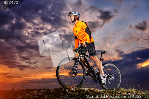 Image of Man in helmet stay on bicycle under sky with clouds.