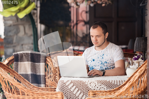 Image of young man working on laptop at the wooden table outdoors