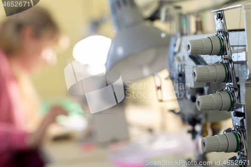 Image of close-up of sewing equipment with threads and a worker in the background