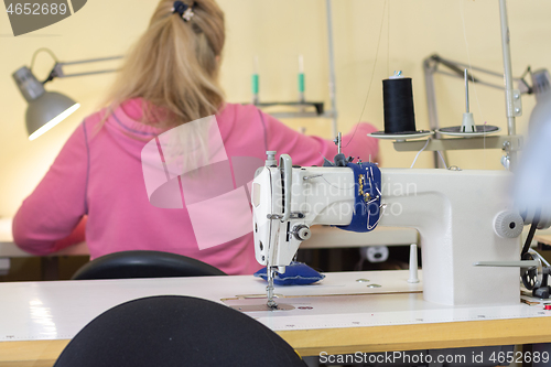 Image of Girl sits with her back and sews on a sewing machine in a sewing shop