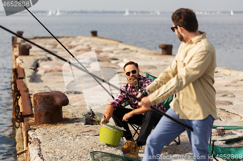 Image of male friends with fishing rods on sea pier