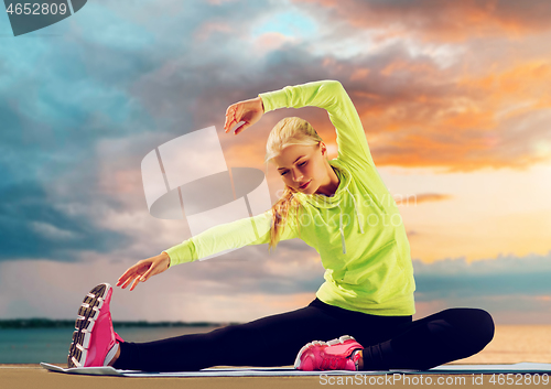 Image of woman stretching on exercise mat at seaside