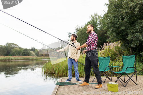 Image of male friends with fishing rods on lake pier