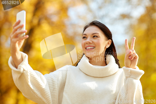 Image of woman taking selfie by smartphone at autumn park