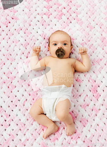 Image of baby girl in diaper lying with pacifier on blanket