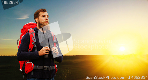 Image of man with backpack and binocular over sunset