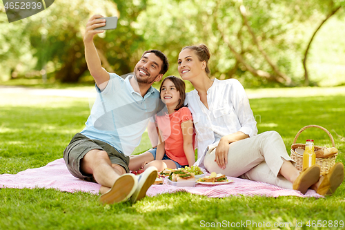 Image of family having picnic and taking selfie at park