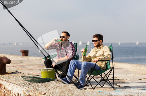 Image of male friends fishing and drinking beer on pier