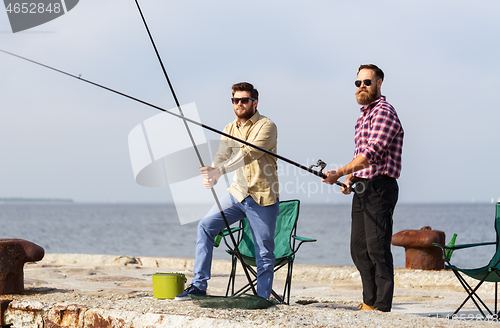 Image of male friends with fishing rods on sea pier