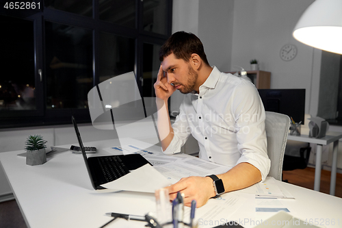 Image of businessman with papers and laptop at night office