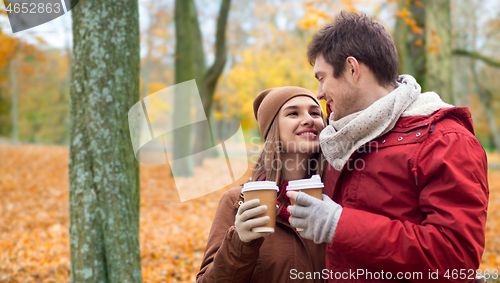 Image of happy couple with coffee walking in autumn park