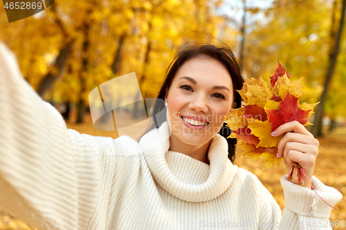 Image of woman with leaves taking selfie in autumn park