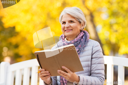 Image of happy senior woman reading diary at autumn park