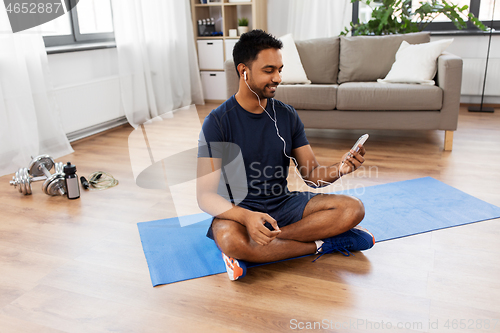 Image of indian man with smartphone on exercise mat at home