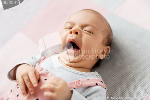 Image of yawning baby girl in pink suit lying on blanket