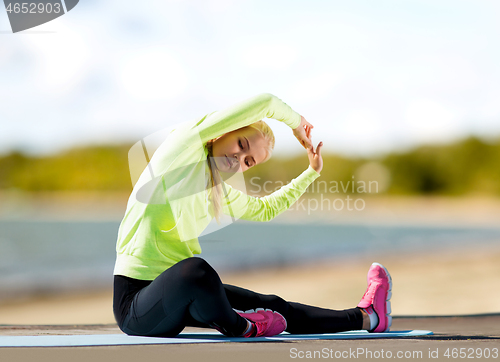 Image of woman stretching on exercise mat on beach