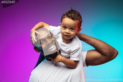 Image of African-american father and son portrait on gradient studio background in neon