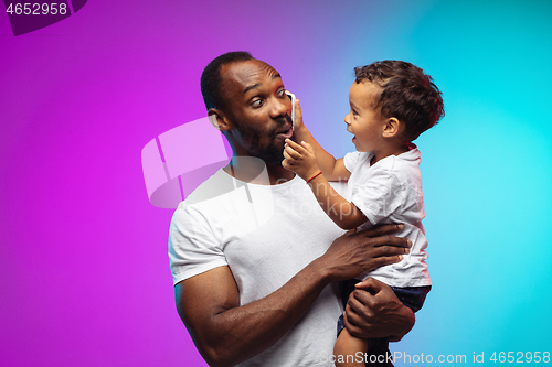 Image of African-american father and son portrait on gradient studio background in neon