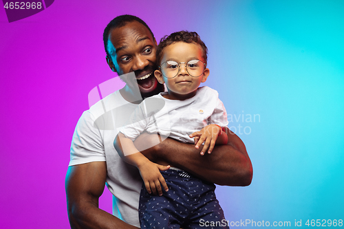 Image of African-american father and son portrait on gradient studio background in neon