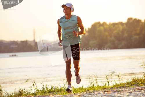 Image of A young athletic man working out listening to the music at the riverside outdoors