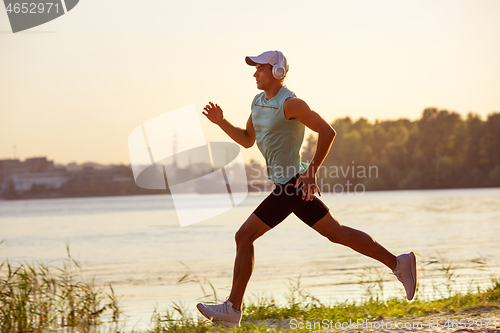 Image of A young athletic man working out listening to the music at the riverside outdoors