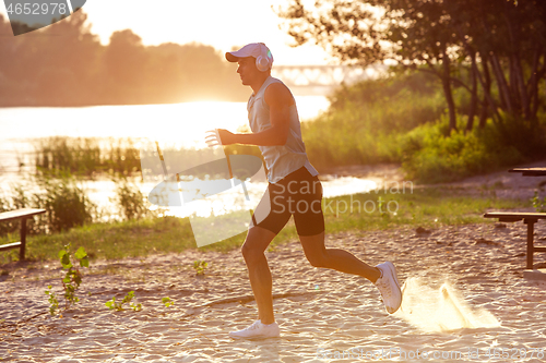 Image of A young athletic man working out listening to the music at the riverside outdoors