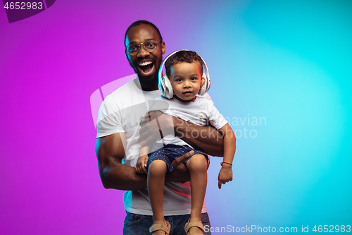 Image of African-american father and son portrait on gradient studio background in neon