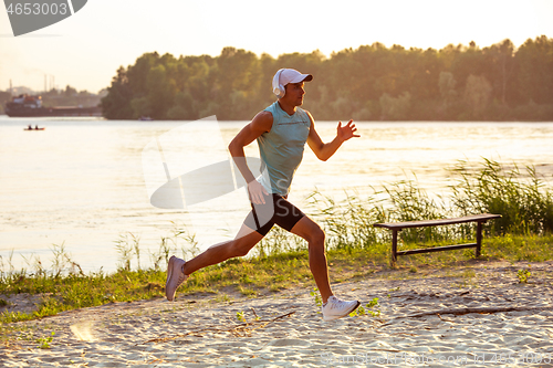 Image of A young athletic man working out listening to the music at the riverside outdoors