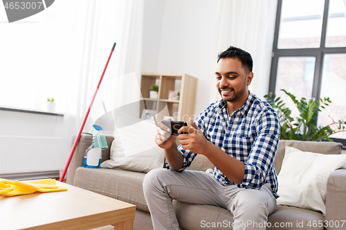 Image of man playing game on smartphone after cleaning home