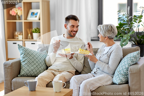 Image of senior mother and adult son eating cake at home