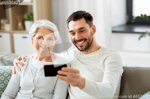 Image of senior mother with adult son taking selfie at home