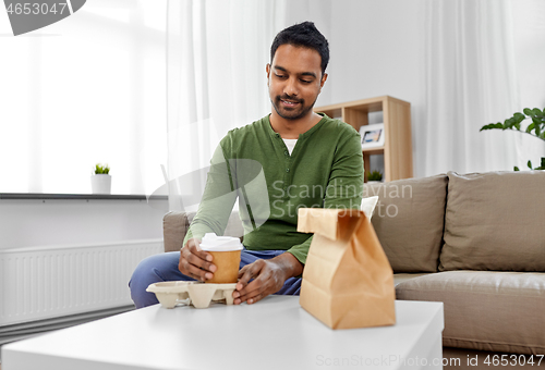 Image of indian man with takeaway coffee and food at home