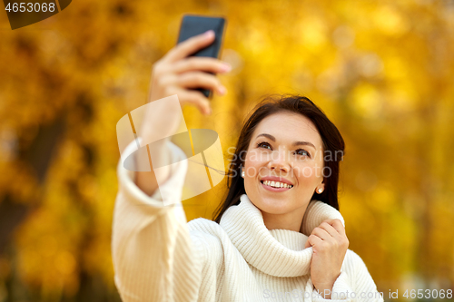 Image of woman taking selfie by smartphone at autumn park