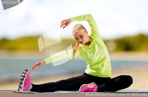 Image of woman stretching on exercise mat on beach