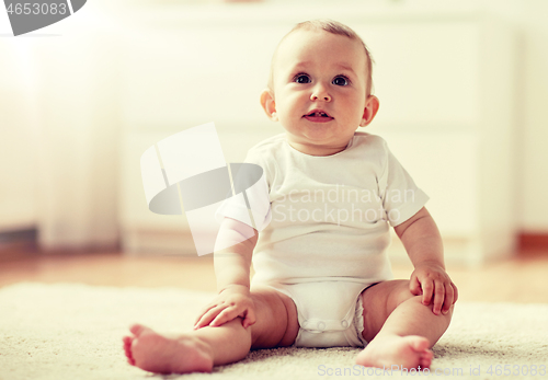 Image of happy baby boy or girl sitting on floor at home