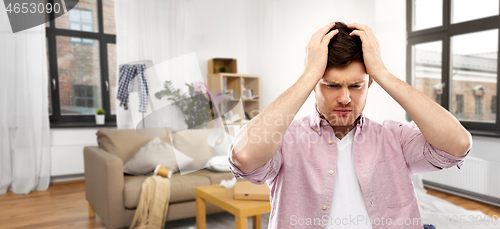 Image of despaired young man in messy room having headache