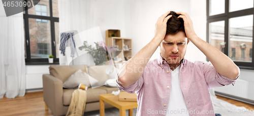 Image of despaired young man in messy room having headache