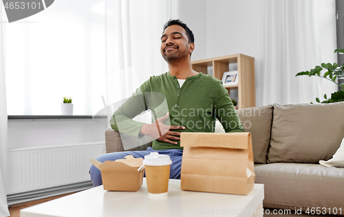 Image of pleased indian man eating takeaway food at home